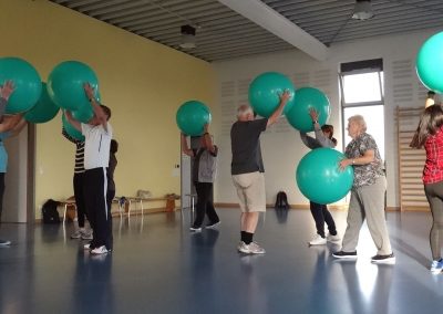 Eine Gruppe von Personen macht Übungen mit dem Gymnastikball über dem Kopf haltend (Foto: Corinna Russow/HKI Erlangen).